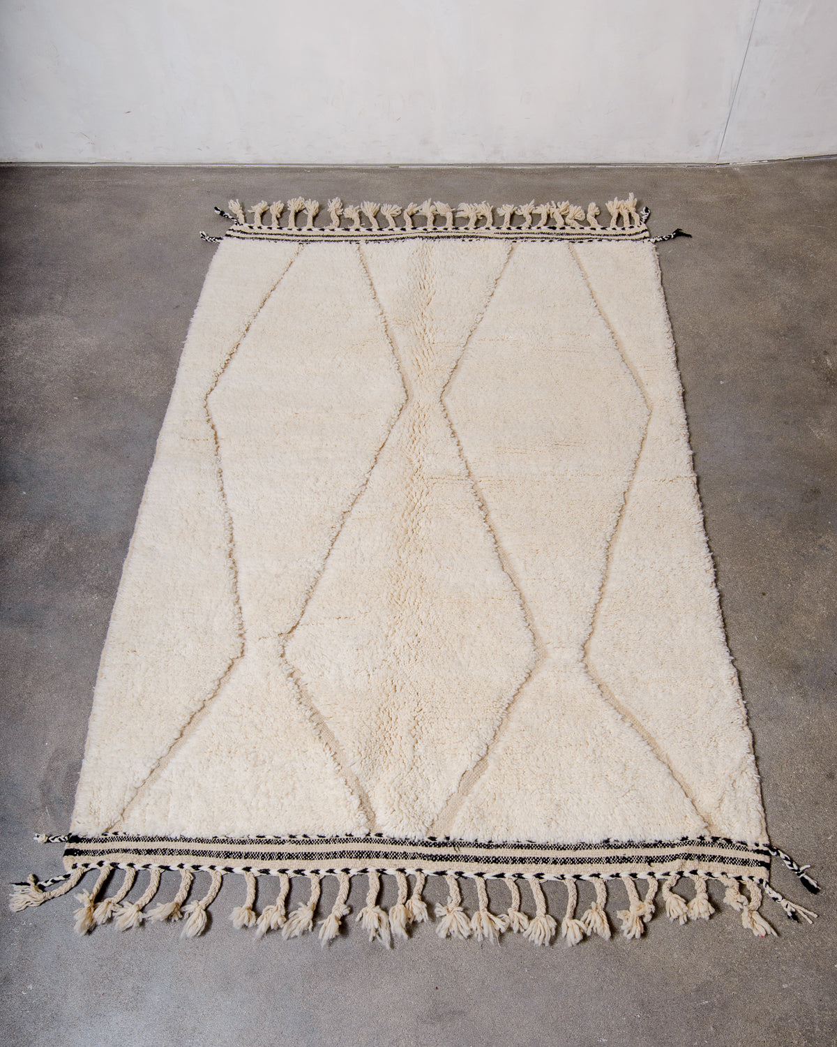 Cream wool rug with design woven in natural wool laying flat on concrete floor.